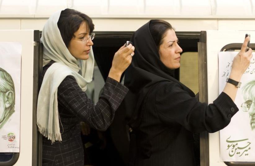 Iranian women take a picture of a presidential candidate with their mobile phones in Tehran , Iran (photo credit: REUTERS)