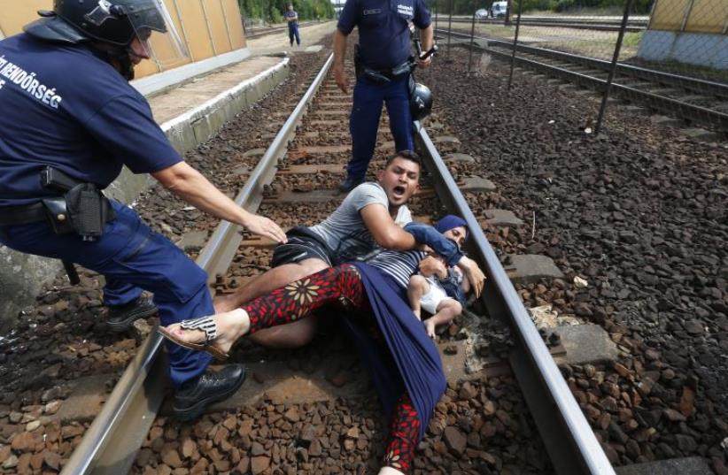 Hungarian policemen stand by the family of migrants as they wanted to run away at the railway station in the town of Bicske (photo credit: REUTERS)