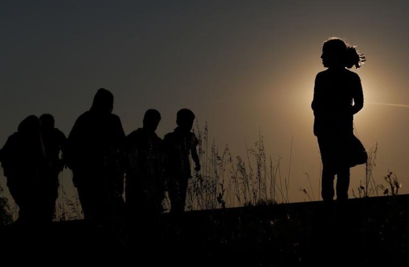 Migrants walk along rail tracks on sunset close to a migrant collection point in Roszke, Hungary (photo credit: REUTERS)