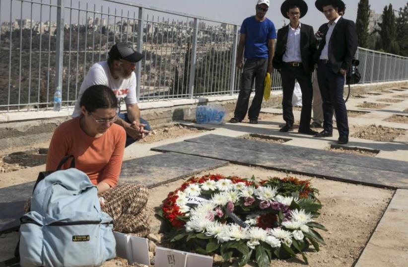 Mourners stand beside the fresh grave of Eitam and Na'ama Henkin after their funeral at a Jerusalem cemetery (photo credit: REUTERS)