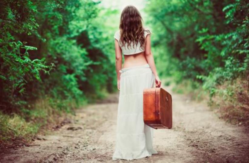 Young woman with suitcase in hand going away by a rural road (photo credit: INGIMAGE)