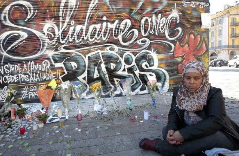 A woman sits by a poster which reads "Solidarity with Paris" in Nice, France, November 15, 2015, after a series of deadly shootings in Paris on Friday. (photo credit: REUTERS)