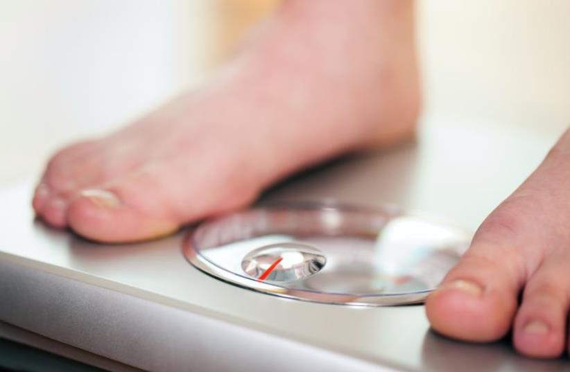 Woman standing on bathroom scale measuring her weight  (photo credit: INGIMAGE)