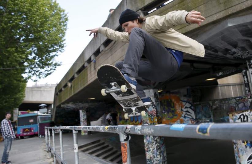 A skateboarder performs a jump over a railing (photo credit: REUTERS)