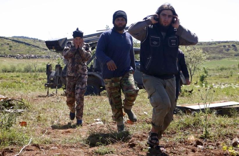 Rebel fighters from the Ahrar al-Sham Islamic Movement cover their ears during the launch of grad rockets from Idlib countryside towards forces loyal to Syria's President Bashar al-Assad, who are stationed at Jureen town in al-Ghab plain in the Hama countryside April 24, 2015. (photo credit: REUTERS)