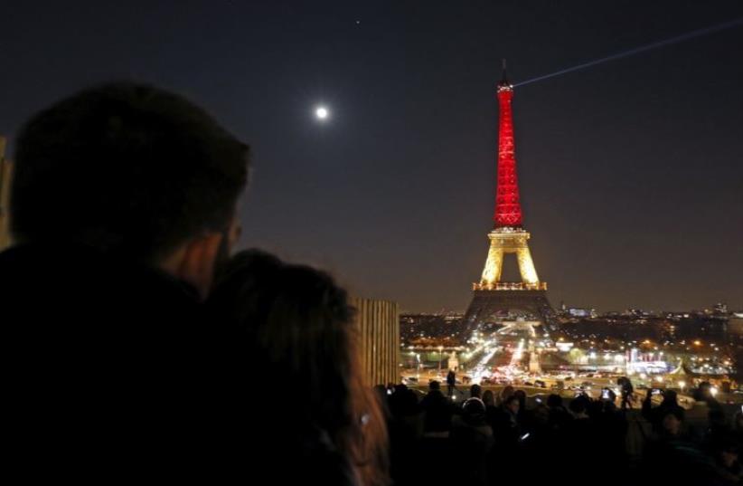 A couple looks at the Eiffel Tower lit up in the colors of the Belgian flag in Paris (photo credit: REUTERS)