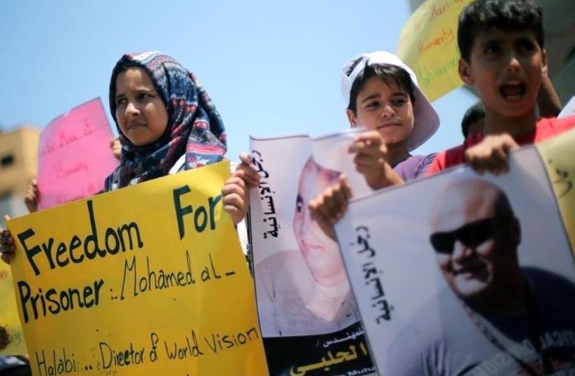 Palestinian demonstrators take part in a protest in solidarity with Mohammad El Halabi, World Vision's manager of operations in Gaza who was accused by Israel of funnelling millions of dollars in aid money to Hamas, organised by foundations and societies benefiting from World Vision in Gaza City Aug (photo credit: REUTERS)