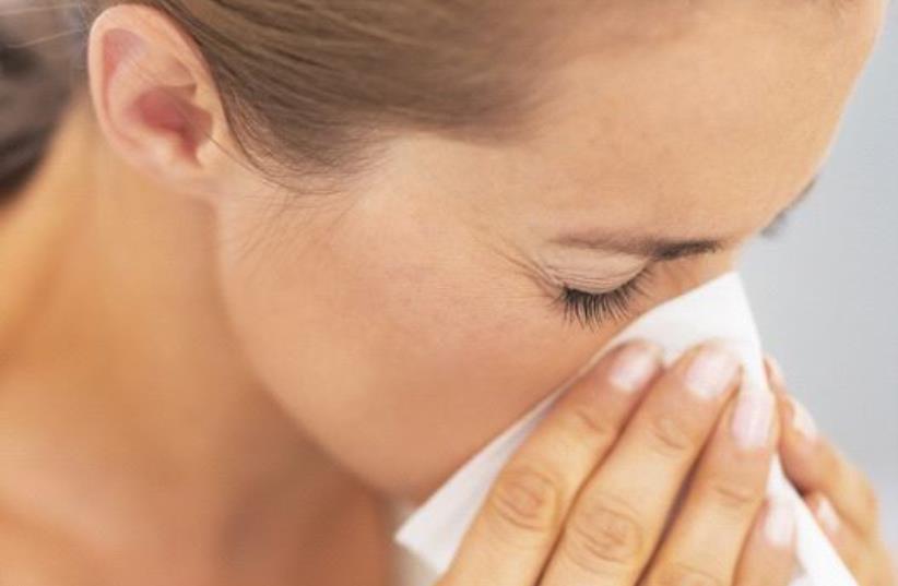 A woman blowing her nose into a tissue, possibly after sneeze or while sick (photo credit: INGIMAGE)