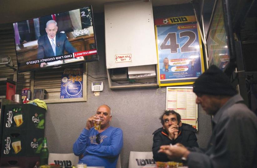 PEOPLE SIT at a kiosk in Ashkelon as a television broadcasts Prime Minister Benjamin Netanyahu’s speech to the US Congress on March 3, 2015. (photo credit: REUTERS)