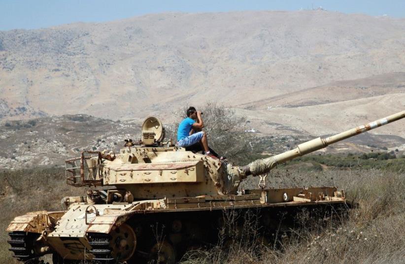 A man sits on an old tank as he watches fighting taking place in Syria from the Israeli side of the border fence (photo credit: REUTERS)