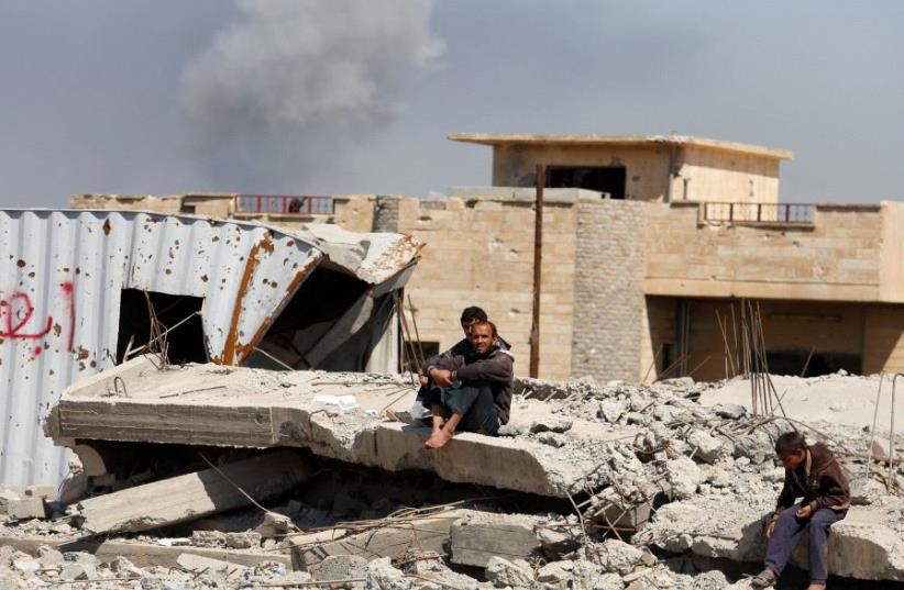 Smoke rises while displaced Iraqis wait to get food supplies as Iraqi forces battle with Islamic State militants, in western Mosul, Iraq March 27, 2017 (photo credit: REUTERS)