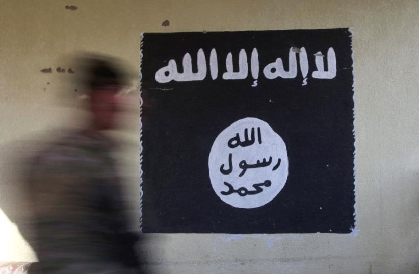  A member of the Iraqi rapid response forces walks past a wall painted with the black flag commonly used by Islamic State militants (photo credit: REUTERS)