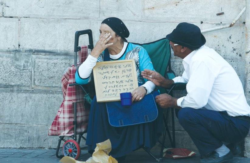 A PASSERBY stops to console a poor woman in Jerusalem in 2015. (photo credit: MARC ISRAEL SELLEM)