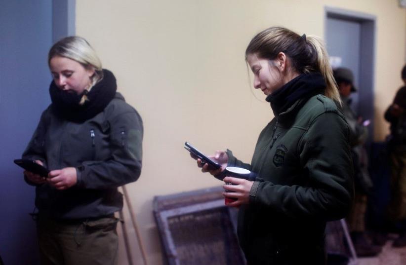 Female Israeli soldiers from the Haraam artillery battalion use their mobile phones as they stand in the women's living quarters at a military base in the Golan Heights March 1, 2017.  (photo credit: REUTERS/NIR ELIAS)