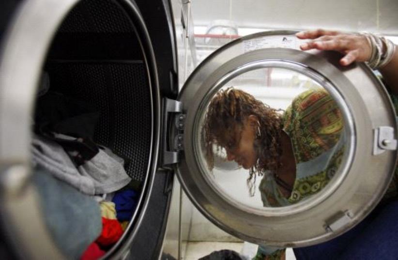 A woman loads laundry into the washing machine at a laundromat in Cambridge, Massachusetts July 8, 2009. (photo credit: REUTERS/BRIAN SNYDER)