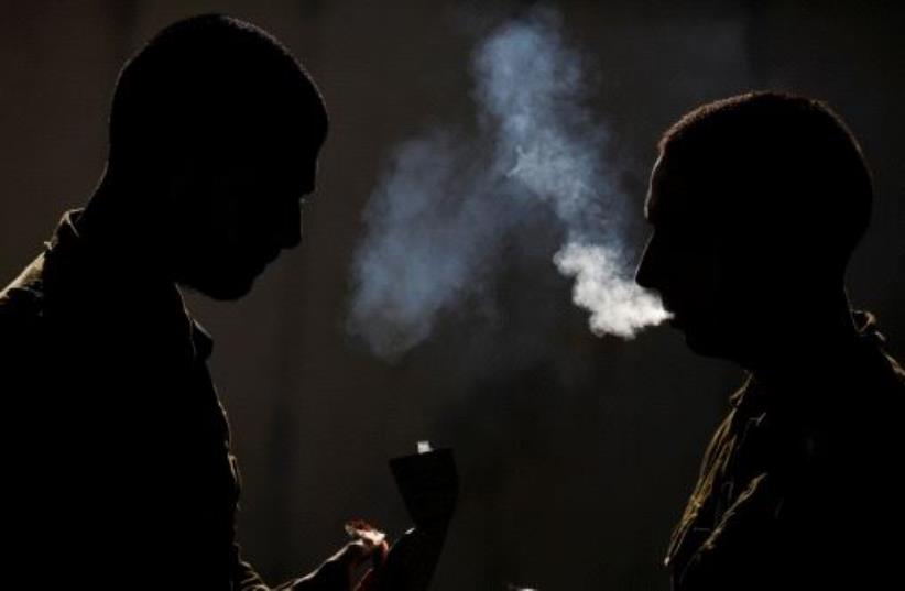 Silhouetted Israeli soldiers from the Home Front Command Unit take a smoking break during an urban warfare drill inside a mock village at Tze'elim army base in Israel's Negev Desert June 11, 2017 (photo credit: REUTERS/AMIR COHEN)