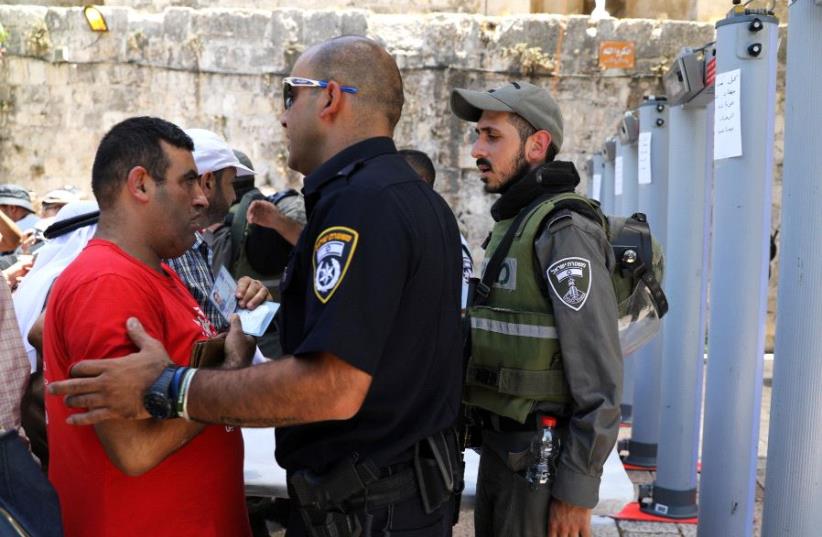 An Israeli police officer checks the identity of a Palestinian man next to newly installed metal detectors at an entrance to the compound known to Muslims as Noble Sanctuary and to Jews as Temple Mount, in Jerusalem's Old City July 16, 2017. (photo credit: AMMAR AWAD / REUTERS)