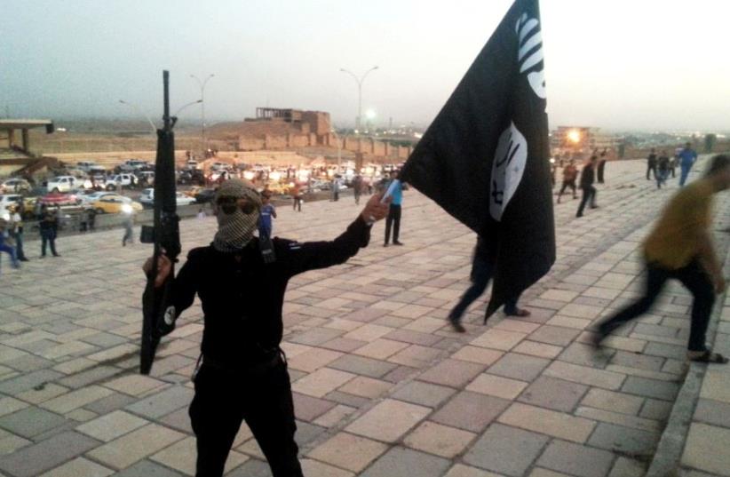 A fighter of the Islamic State of Iraq and the Levant (ISIL) holds an ISIL flag and a weapon on a street in the city of Mosul June 23, 2014. (photo credit: REUTERS/STRINGER)