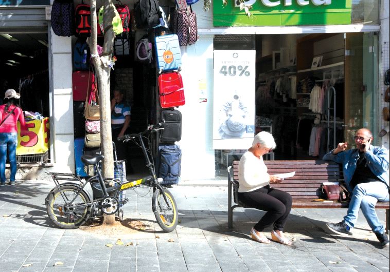 People sit on a bench in a Jerusalem while next to them a bicycle is latched onto a tree (photo credit: MARC ISRAEL SELLEM)