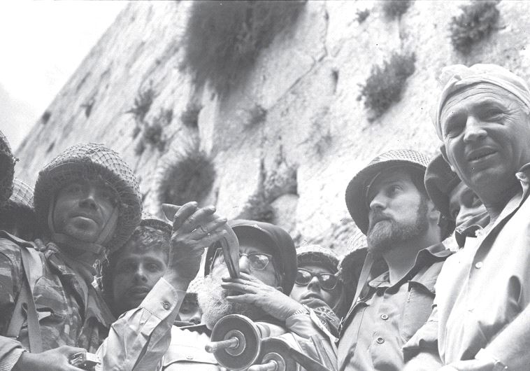 IDF CHIEF RABBI Shlomo Goren blows a shofar while he clutches a Torah scroll at the Western Wall on the day Jerusalem was reunified in June 1967 (credit: GPO)