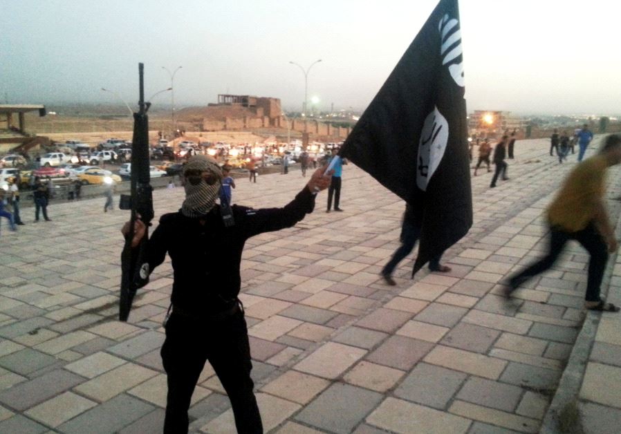 A fighter of the Islamic State of Iraq and the Levant (ISIL) holds an ISIL flag and a weapon on a street in the city of Mosul June 23, 2014. (credit: REUTERS/STRINGER)