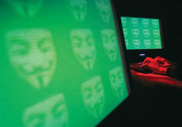 The logo for the cyber hacking group ‘Anonymous’ is seen on computer screens.