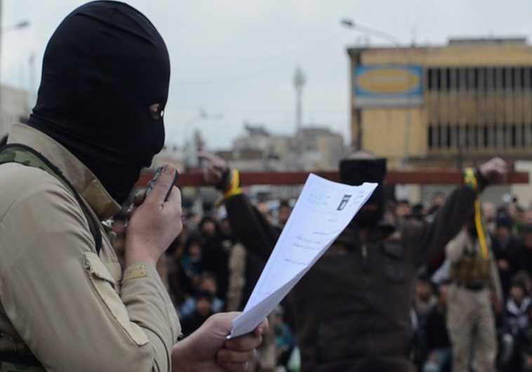 A masked Islamic State militant reads the charges of two men tied to a cross