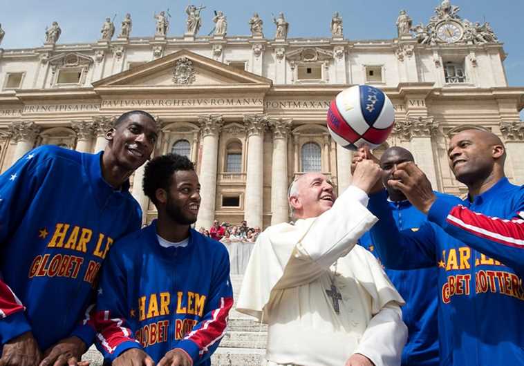 Pope Francis smiles as he plays with a basketball next to a member of the Harlem Globetrotters 