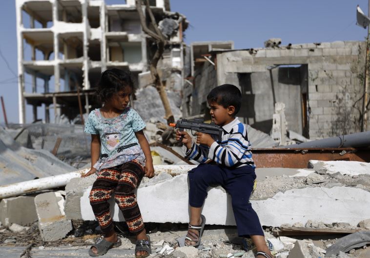 Palestinian children play with a toy gun in front of homes ruined during Israel's bombardment in 2014