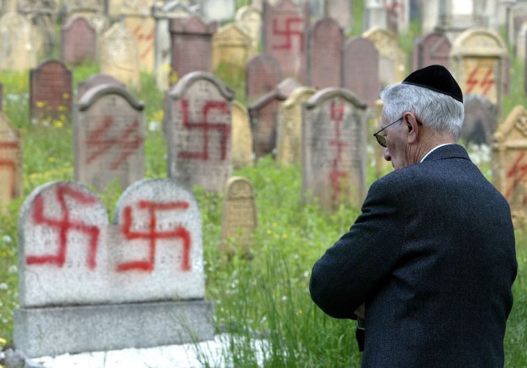A Jewish man stands near some of the 127 graves desecrated by vandals with Nazi swastikas and anti-semitic slogans in the Jewish cemetery of Herrlisheim 