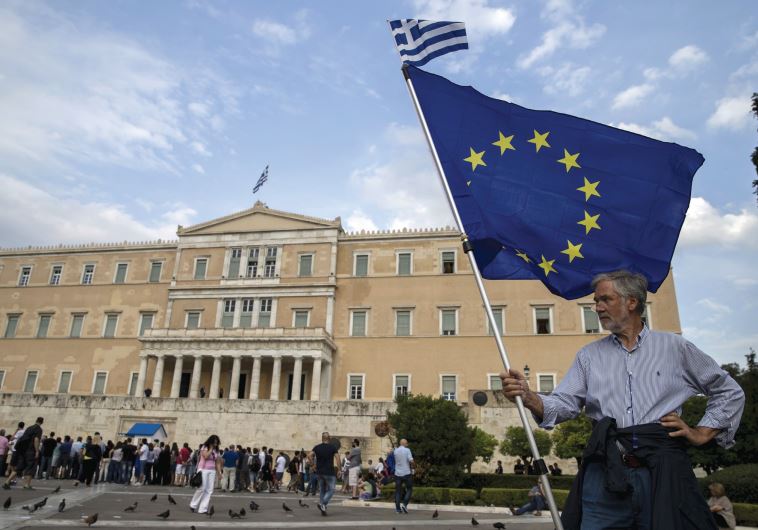 A pro-euro protester holds a European Union flag with a Greek national flag on top during a rally in front of the parliament building in Athens