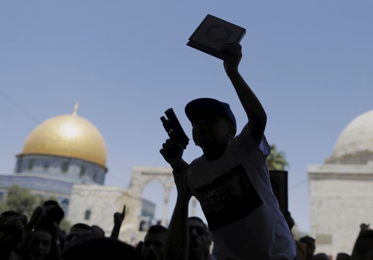 A Palestinian youth is silhouetted as he holds a toy gun and a Koran during a protest after Friday prayers on Temple Mount in Jerusalem's Old City