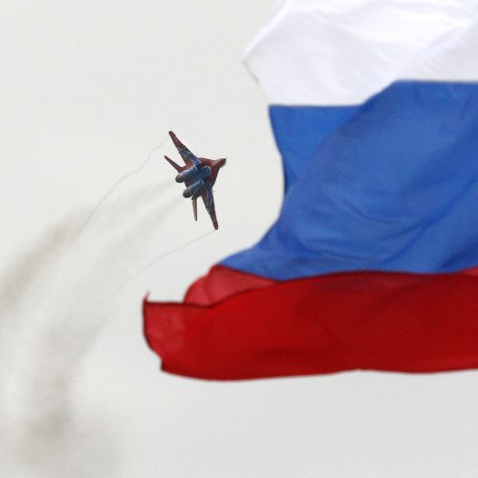 A MiG-29 fighter jet performs a manoeuvre as the Russian national flag flies in the foreground