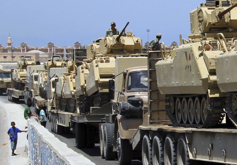 A boy walks near army trucks carrying tanks and vehicles, expecting opposition against militants, arriving at Rafah city.