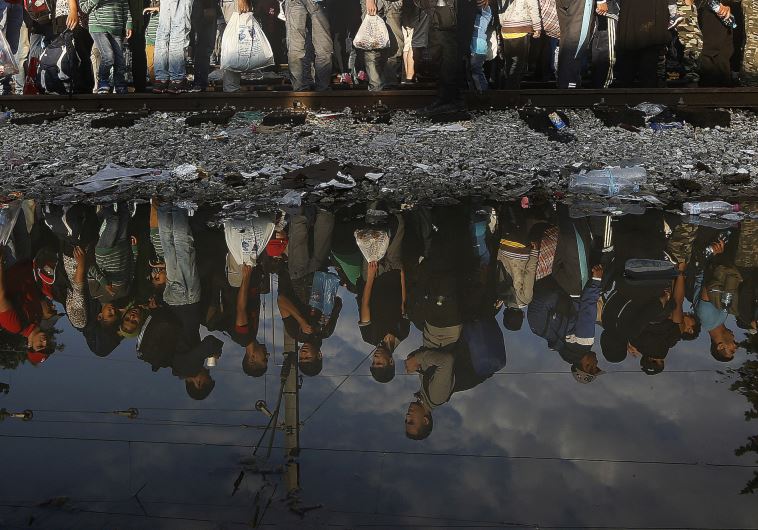 Syrian refugees are reflected in a puddle as they wait for their turn to enter Macedonia at Greece's border