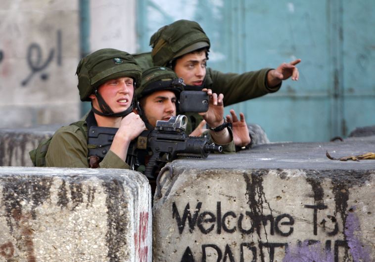 An Israeli soldier uses his mobile to take pictures during clashes with Palestinian stone-throwers in the West Bank city of Hebron March 6, 2015