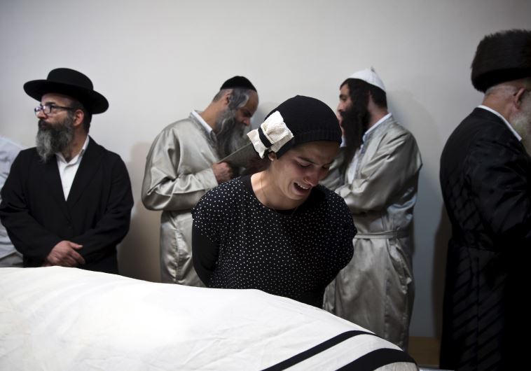 A relative of Aharon Banita mourns next to his covered body before his funeral in Jerusalem