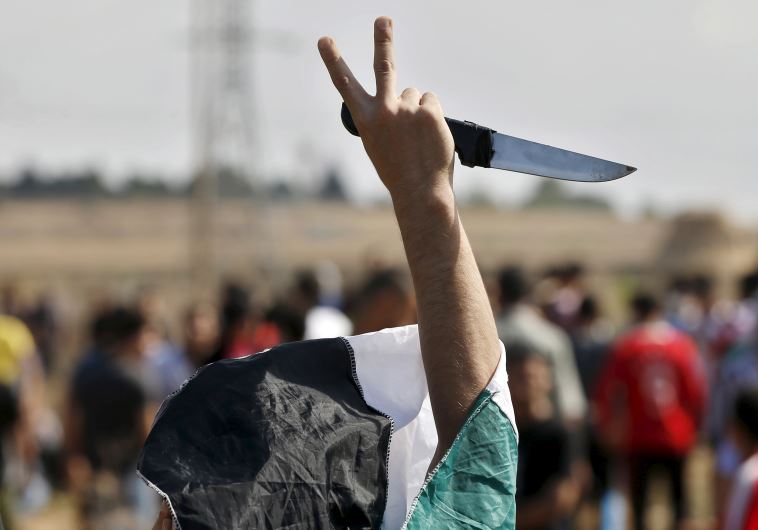 A masked Palestinian protester holds a knife during a protest near the Israeli border fence in northeast Gaza