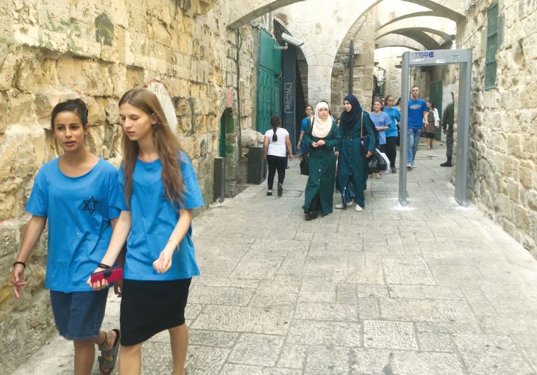 Muslim and Jewish women walk past one of the newly installed metal detectors in the Old City