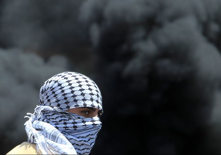 A masked Palestinian protester looks on amid the smoke of burning tires during clashes with Israeli security forces near Nablus