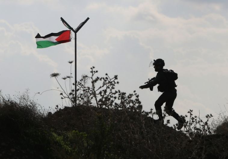 A member of the Israeli security forces runs past a Palestinian flag during clashes with Palestinian stone throwers in the West Bank town of Tul Karm