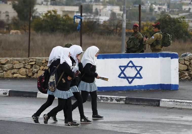 PALESTINIAN SCHOOL girls walk past Israeli soldiers at a checkpoint at a entrance to the village of Beit Einun near Hebron