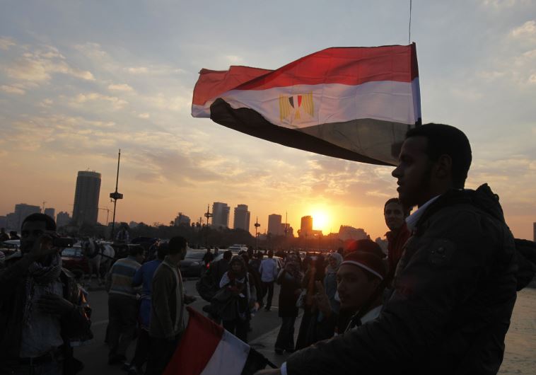 People stand on a bridge overlooking the river Nile as many Egyptians walk on the streets with Egyptian flags in Cairo