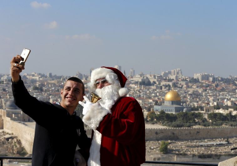 A man takes a selfie with Israeli-Arab Issa Kassissieh as he wears a Santa Claus costume during an annual Christmas tree distribution by the Jerusalem municipality on the Mount of Olives