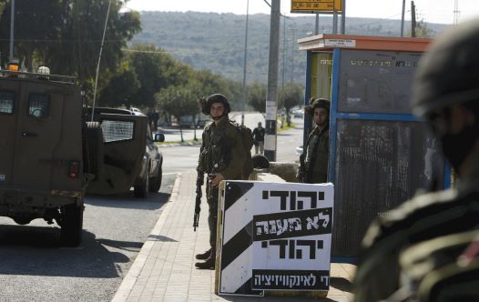 IDF SOLDIERS stand guard next to a poster which reads in Hebrew, ‘A Jew doesn’t torture a Jew. Enough with the inquisition,’ at the entrance to Ariel