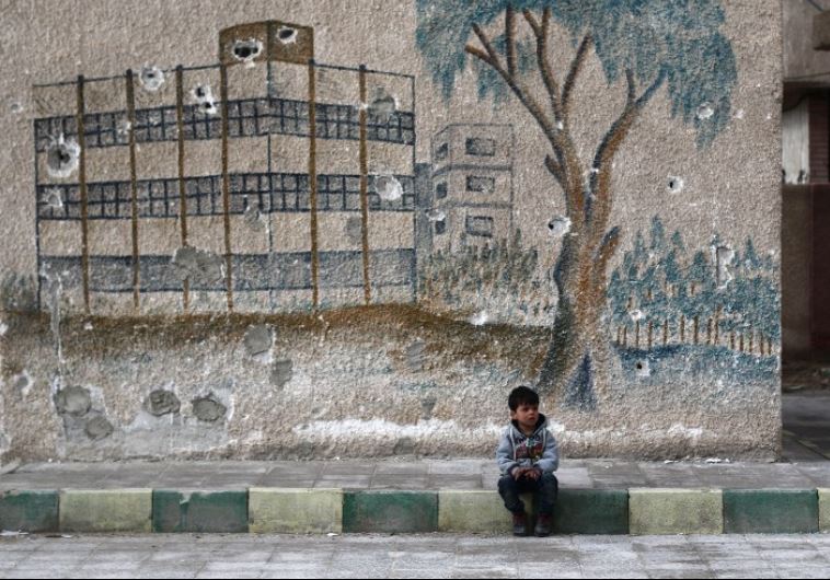 A Syrian child sits in front of a mural covered in bullet holes on the wall of a former school in the rebel-held region of Eastern Ghouta