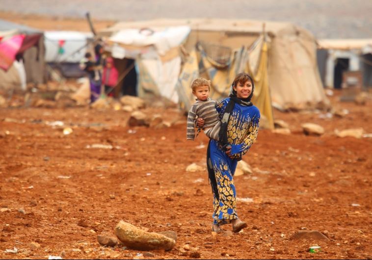 An internally displaced Syrian youth carries a baby inside a refugee camp in the Hama countryside