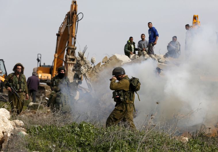 An Israeli soldier reacts to tear gas during the demolition of a Palestinian house at the order of the Israeli army as Palestinians try to stop the demolition in the West Bank village of Biet Ula, west of Hebron January 21, 2016