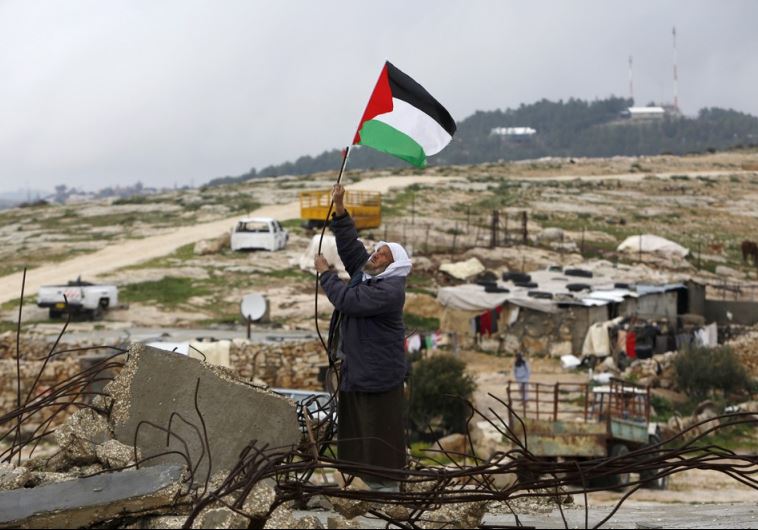 A Palestinian man hangs a Palestinian flag atop the ruins of a mosque, during a snow storm in West Bank village of Mufagara