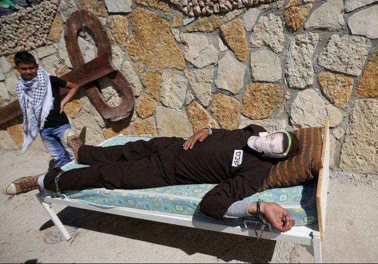 A Palestinian lies on a bed as he covers his face with a picture of Palestinian journalist Mohammad al-Qiq, who was detained by Israeli forces in November and is on an almost-three-month hunger strike